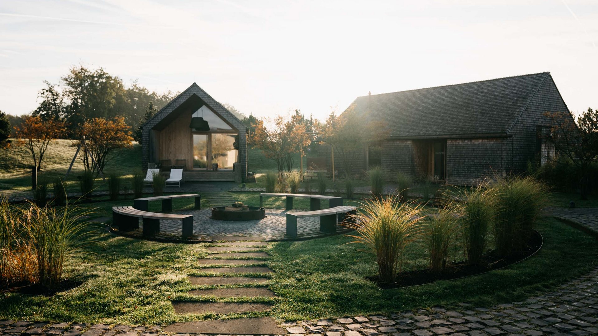 Path leading to two houses with seating area and garden in the morning sun