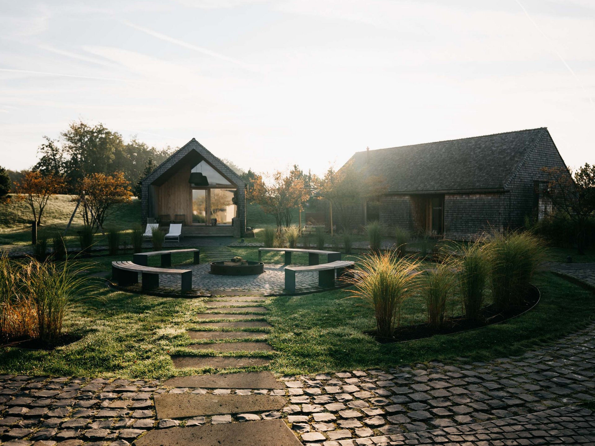 Weg zu zwei Häusern mit Sitzbereich und Garten in der Morgensonne