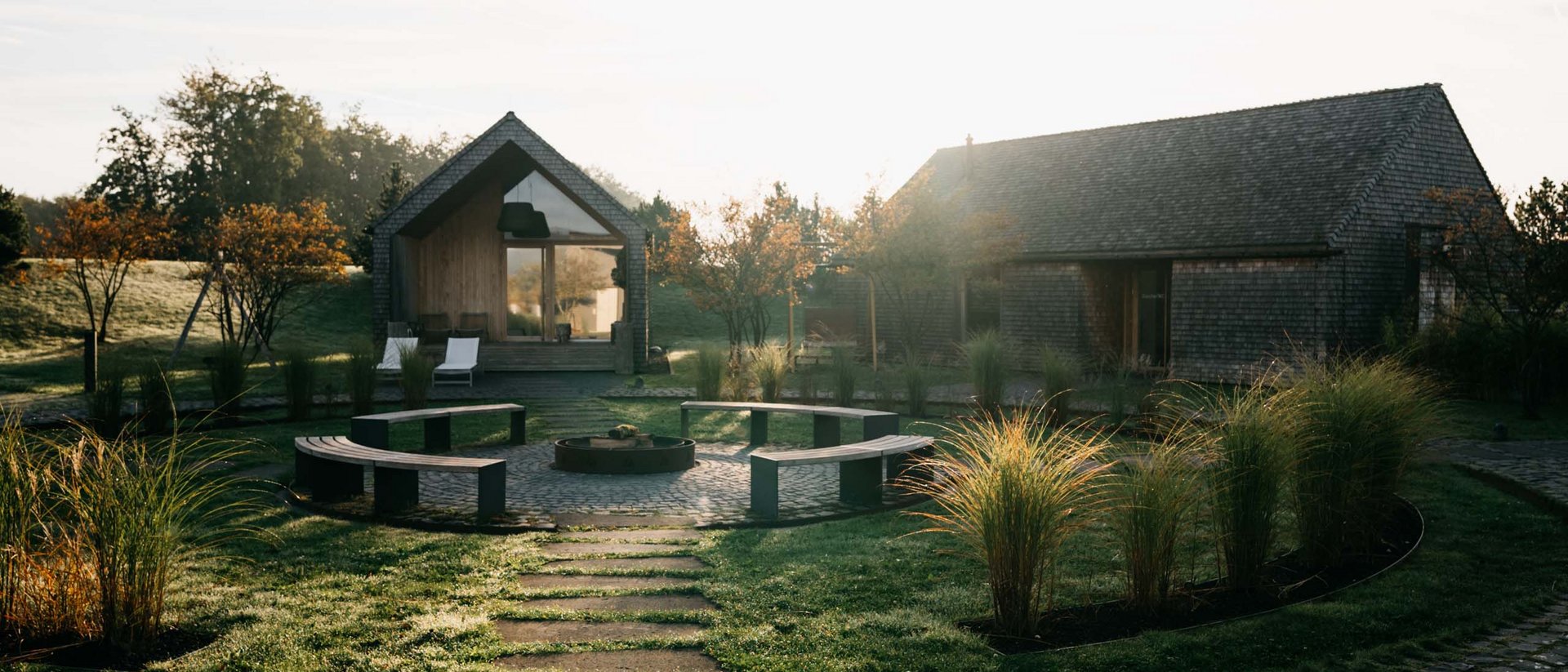 Path leading to two houses with seating area and garden in the morning sun