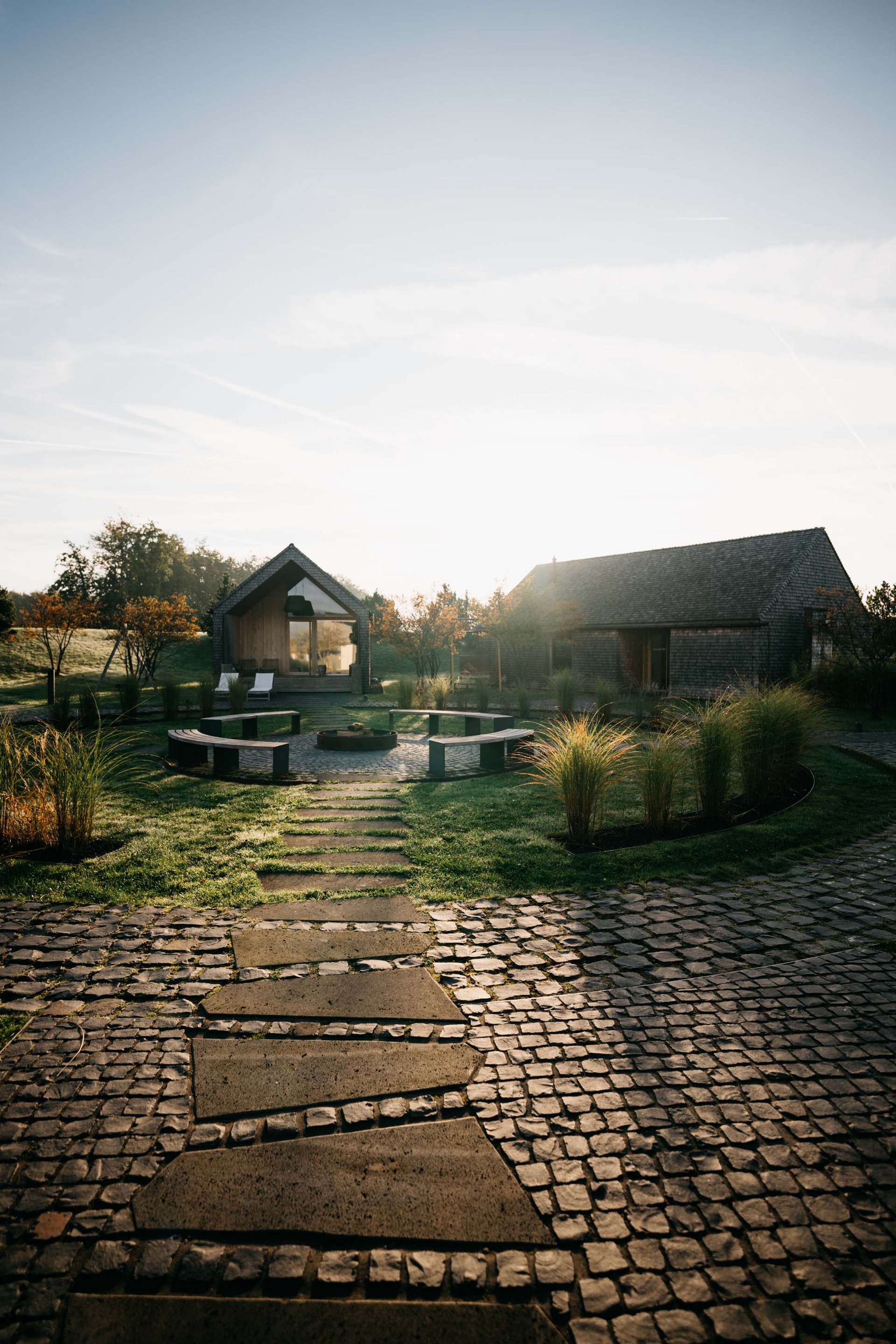 Path leading to two houses with seating area and garden in the morning sun