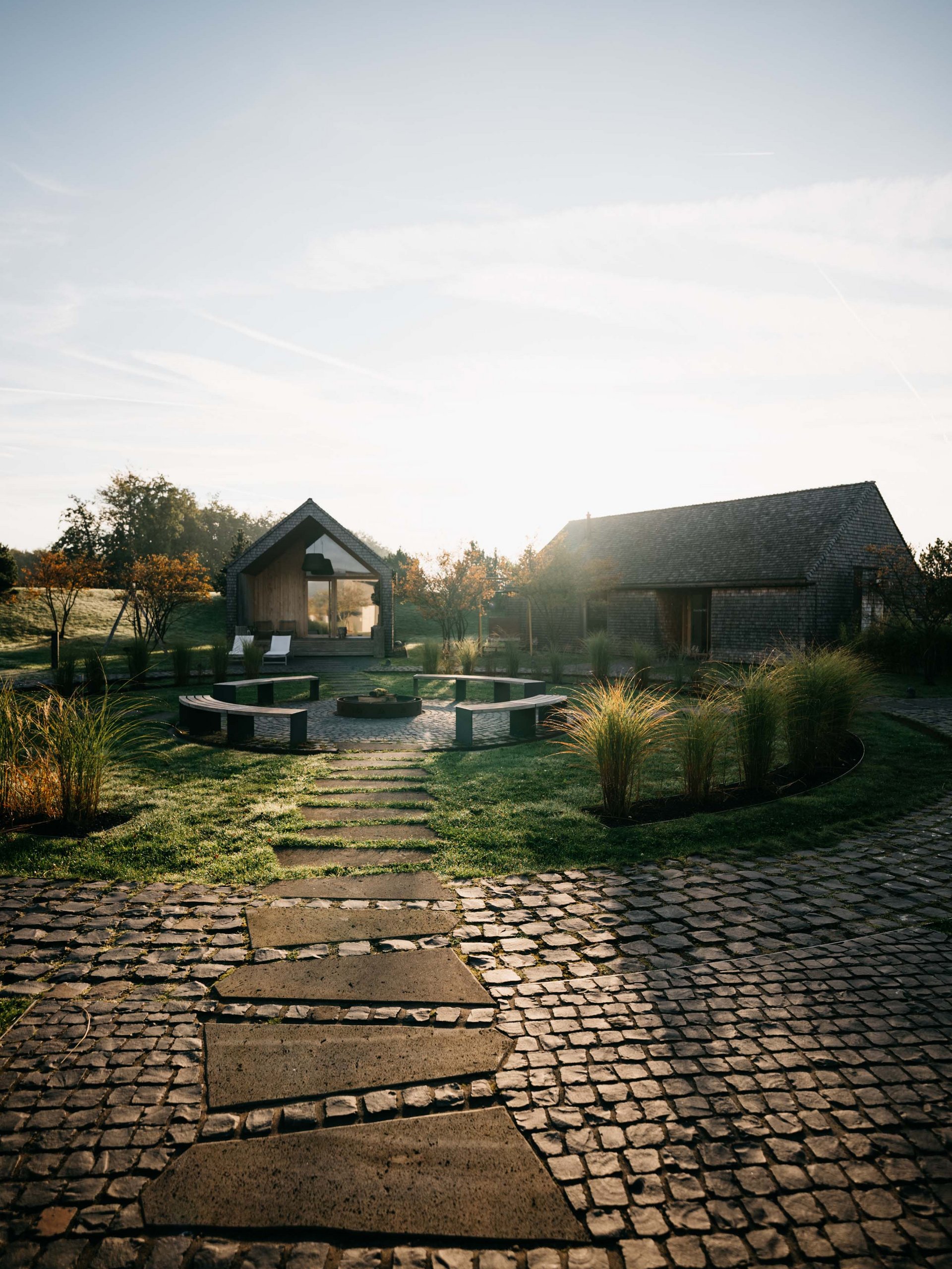 Path leading to two houses with seating area and garden in the morning sun