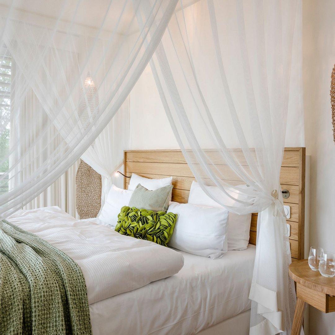 Gemütliches Bett mit Holzrahmen, weißen Vorhängen und grünem Kissen im Hotelzimmer