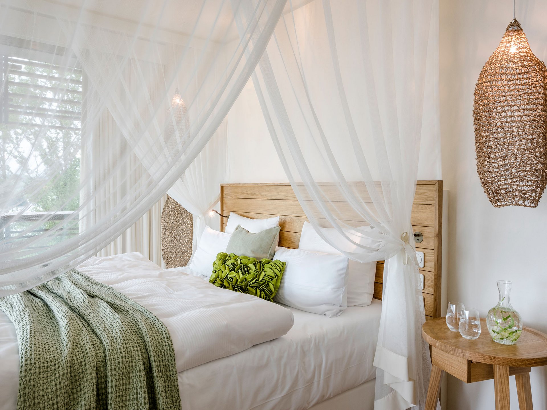 Gemütliches Bett mit Holzrahmen, weißen Vorhängen und grünem Kissen im Hotelzimmer