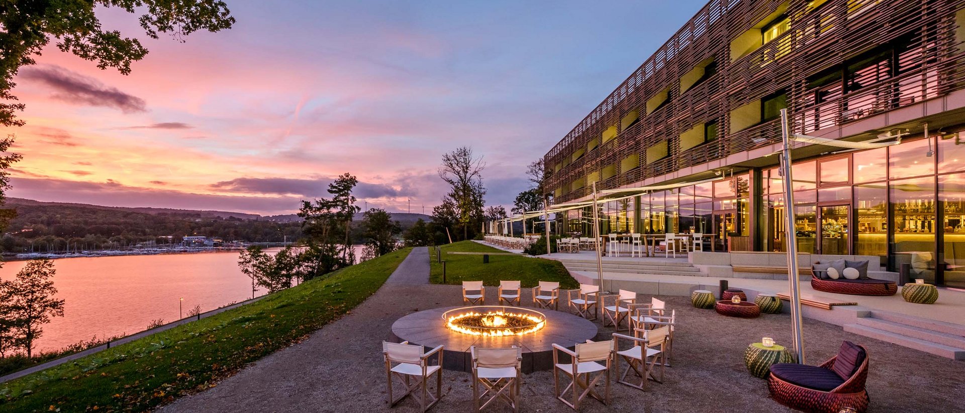 Seating area with fire pit beside modern building and river at sunset
