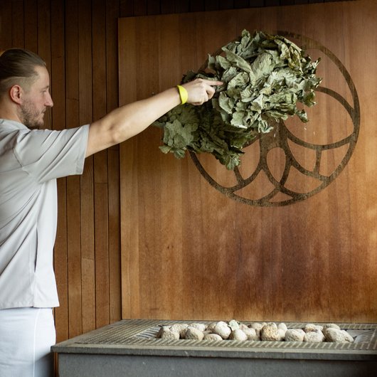 Man waving birch branches in sauna in front of stove