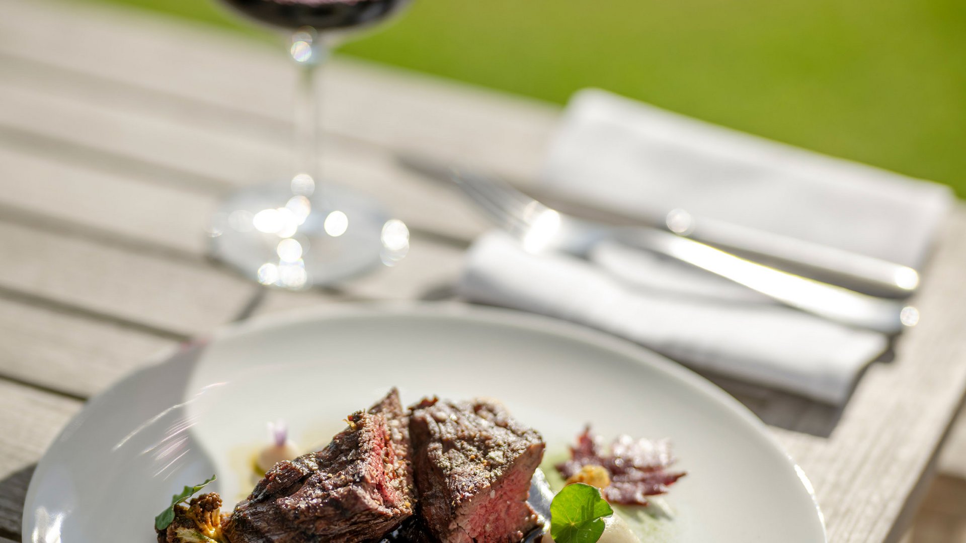 Steak avec légumes sur assiette blanche et verre de vin rouge en plein air