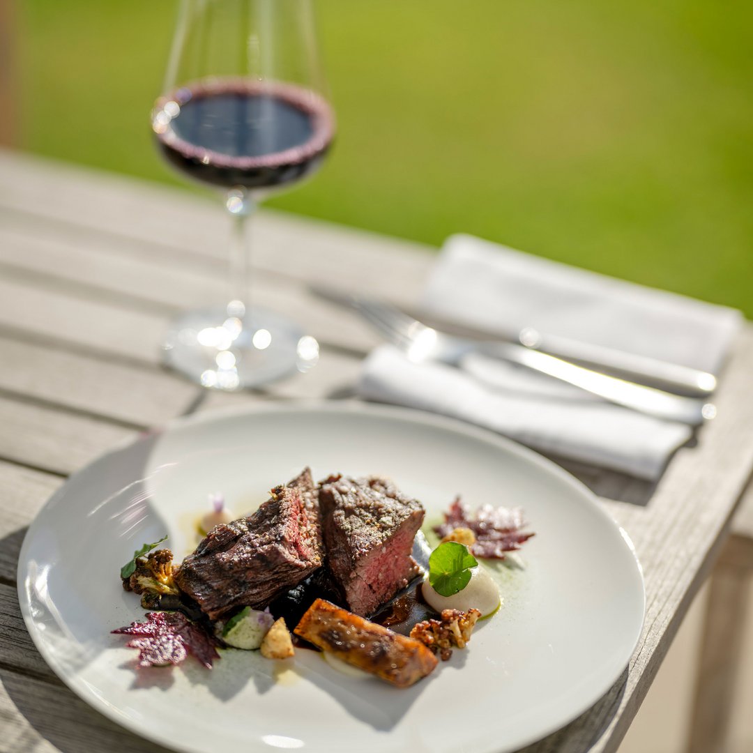 Steak mit Gemüse auf weißem Teller und Glas Rotwein im Freien