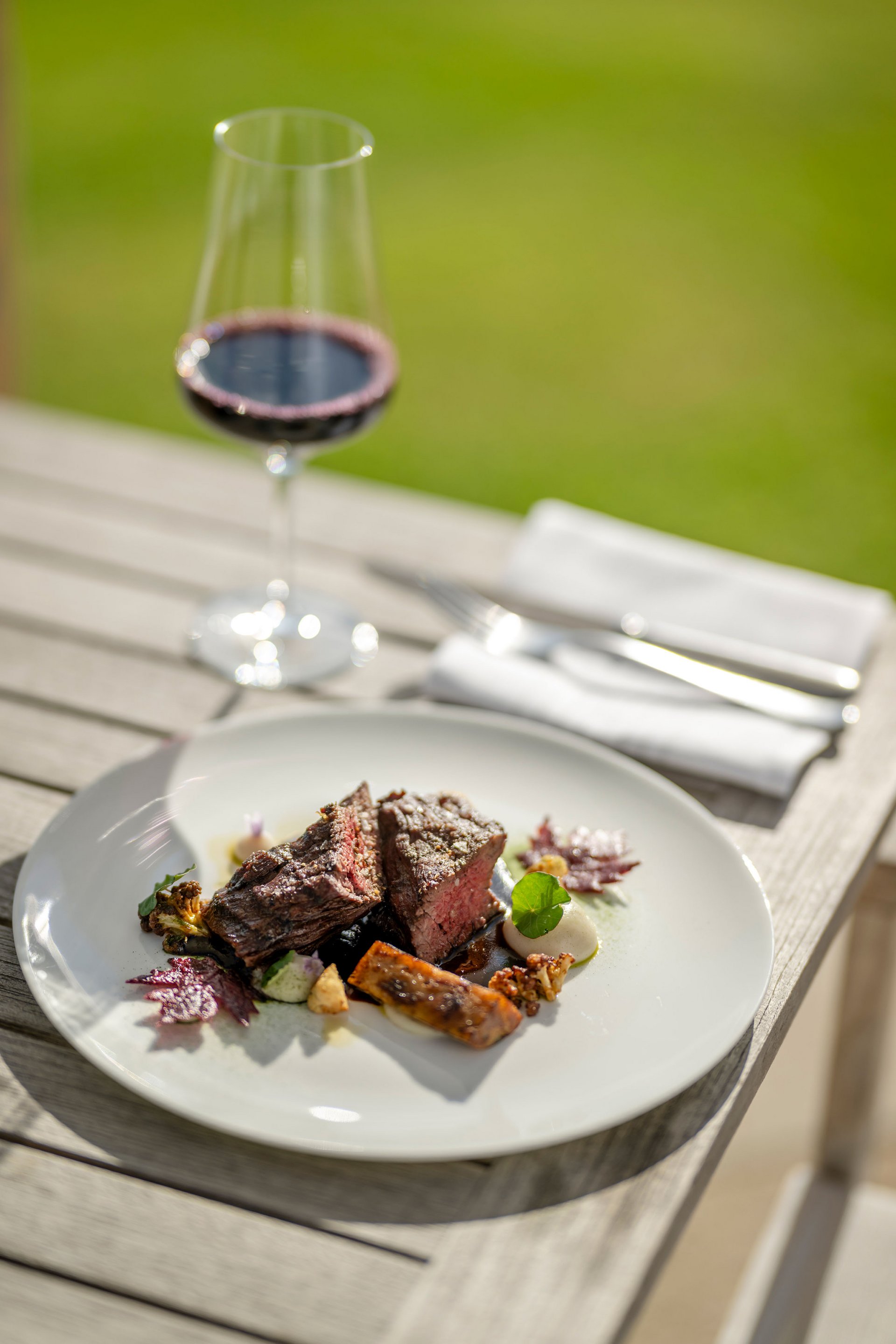 Steak avec légumes sur assiette blanche et verre de vin rouge en plein air