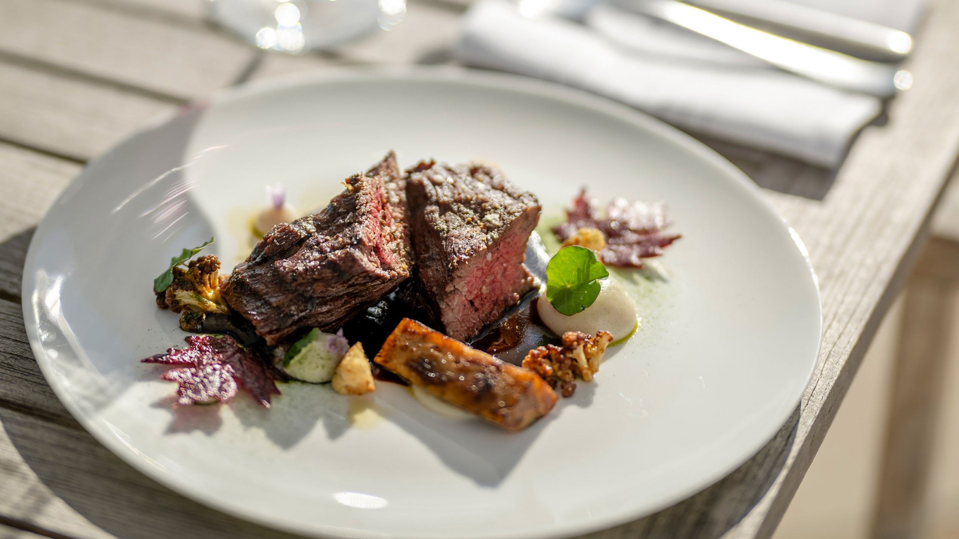 Steak with vegetables on white plate and glass of red wine outdoors
