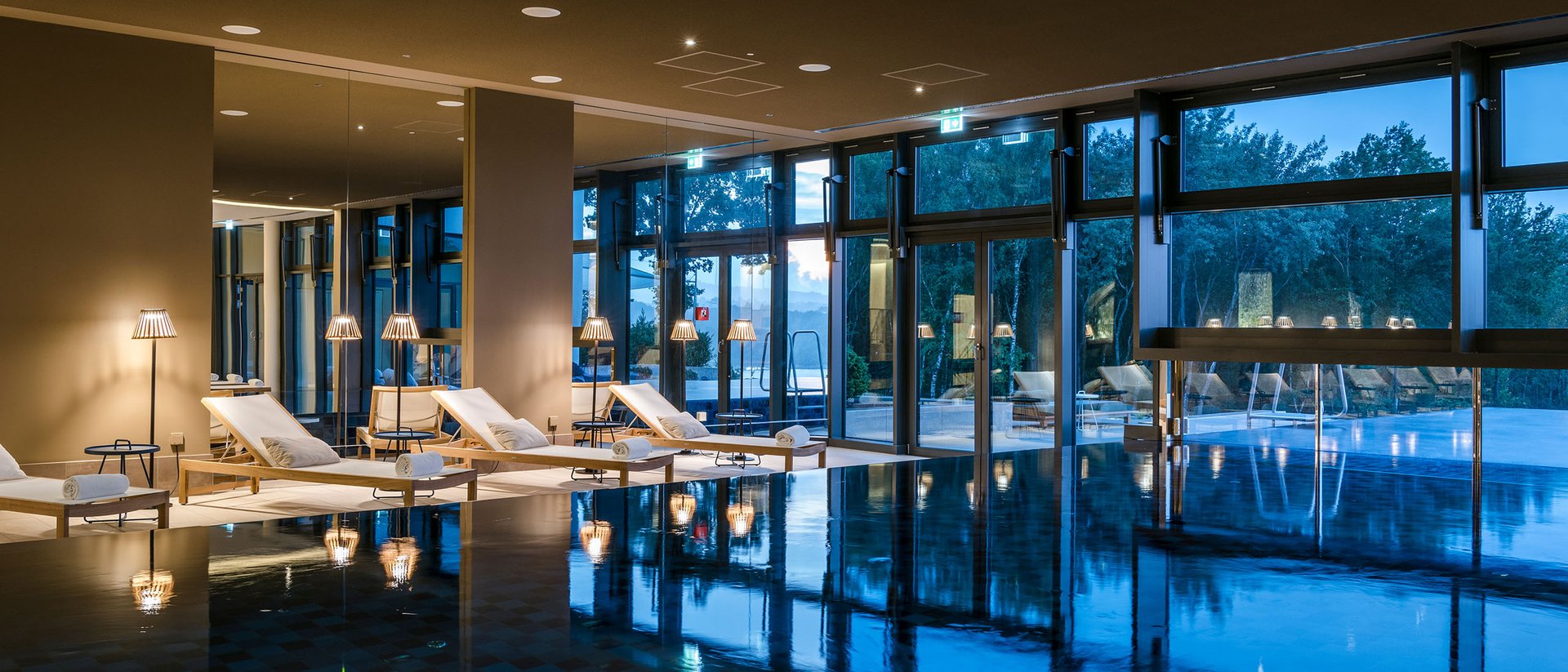 Piscine intérieure avec chaises longues et grandes fenêtres au crépuscule