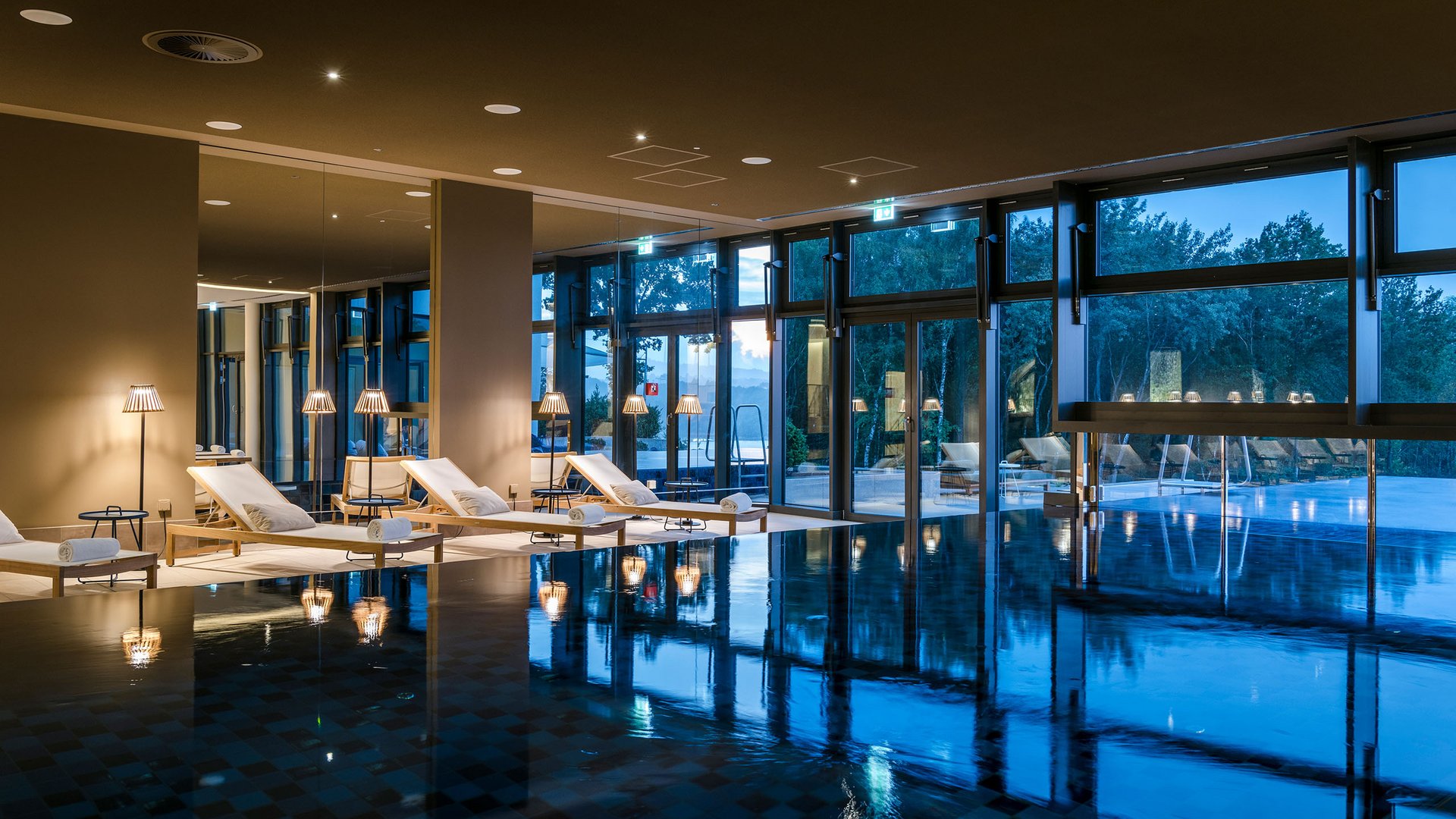 Piscine intérieure avec chaises longues et grandes fenêtres au crépuscule