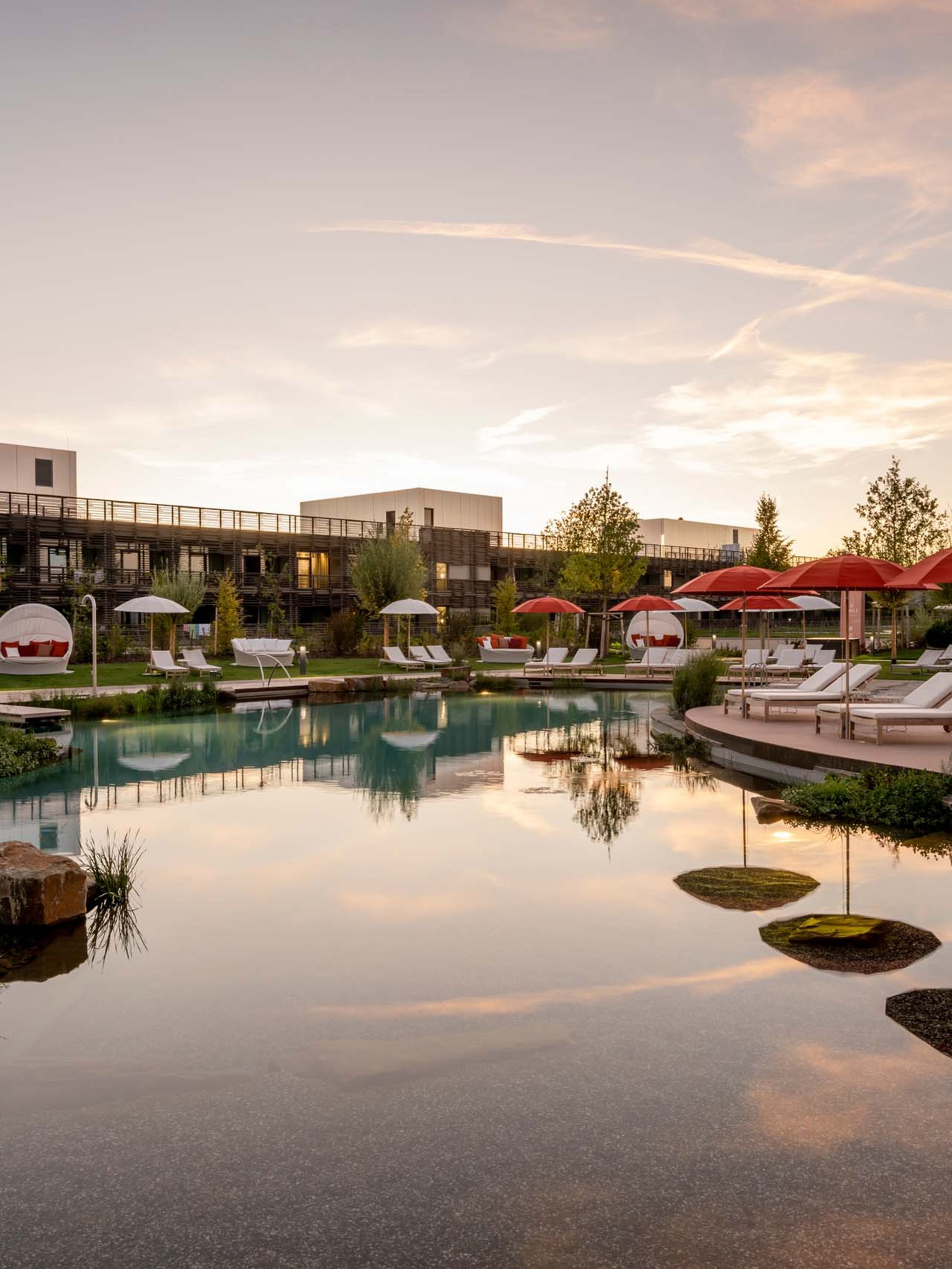 Hotel pool with loungers and red umbrellas at sunset