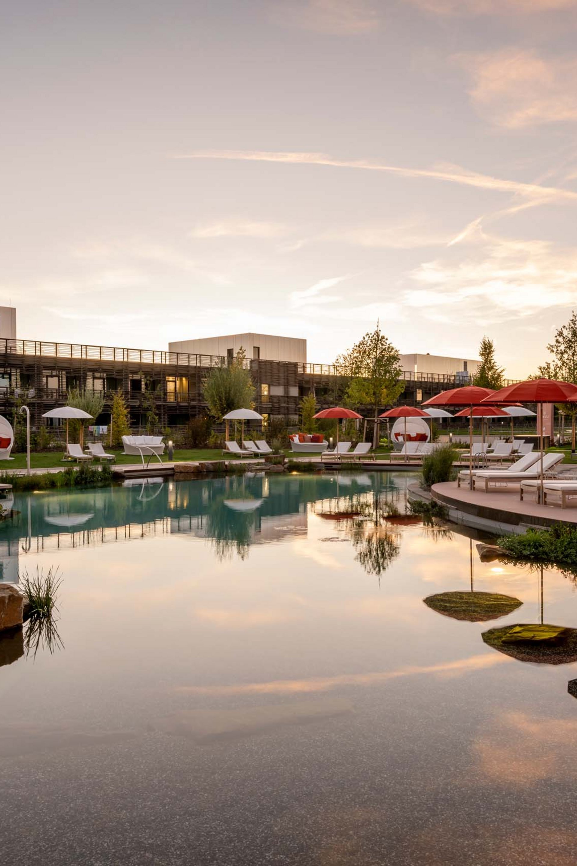 Hotelpool mit Liegen und roten Sonnenschirmen bei Sonnenuntergang