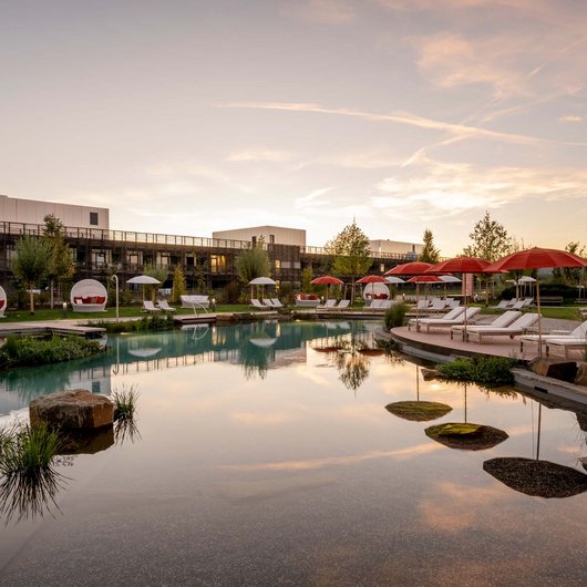 Hotelpool mit Liegen und roten Sonnenschirmen bei Sonnenuntergang