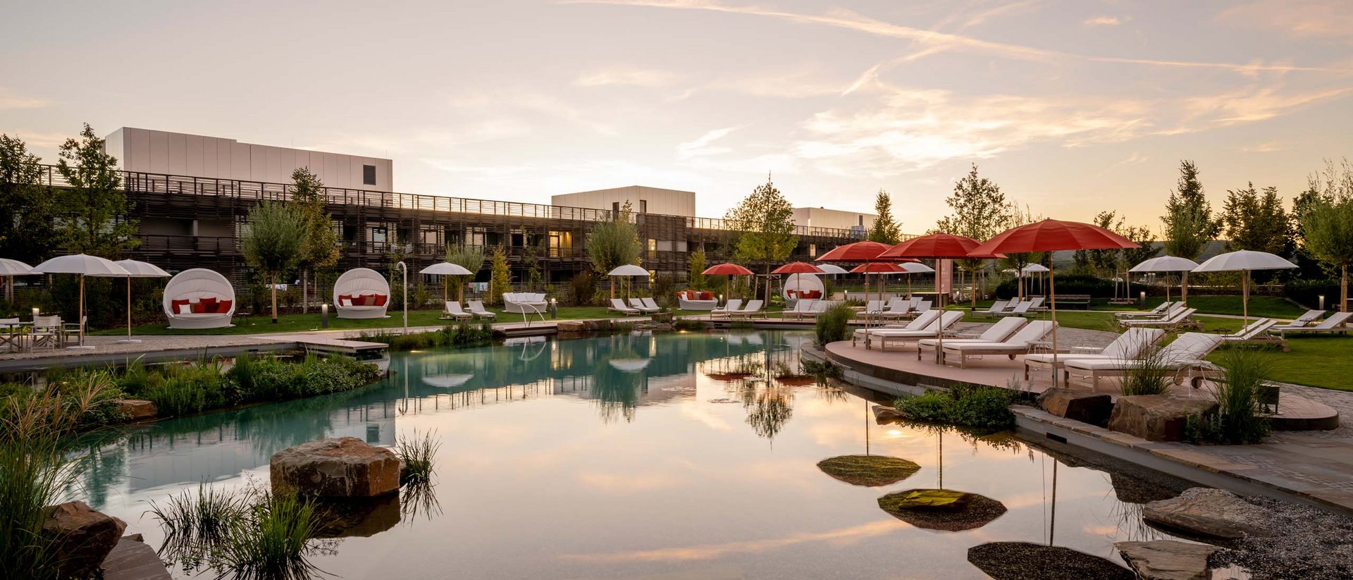 Hotelpool mit Liegen und roten Sonnenschirmen bei Sonnenuntergang