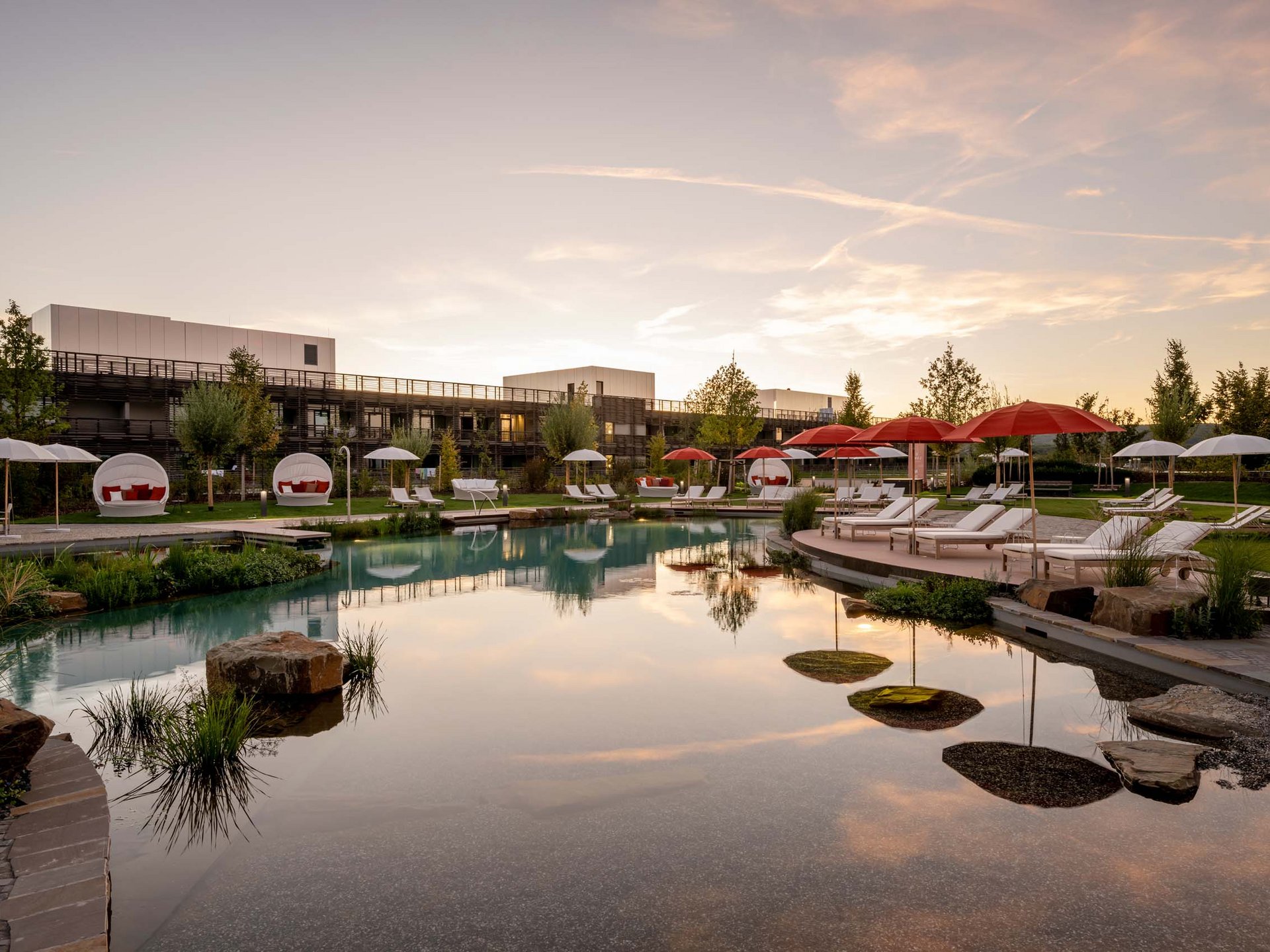 Hotel pool with loungers and red umbrellas at sunset
