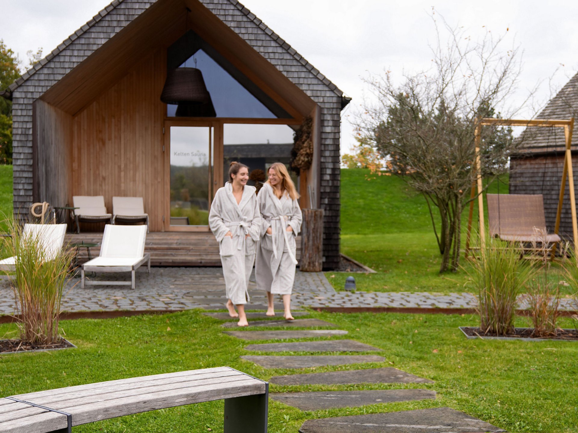 Zwei Frauen in Bademänteln vor einer modernen Sauna im Grünen