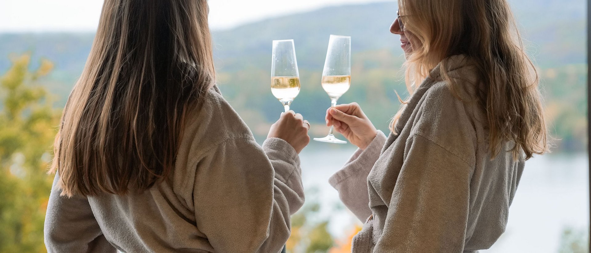 Two women in robes toasting with wine glasses on a balcony