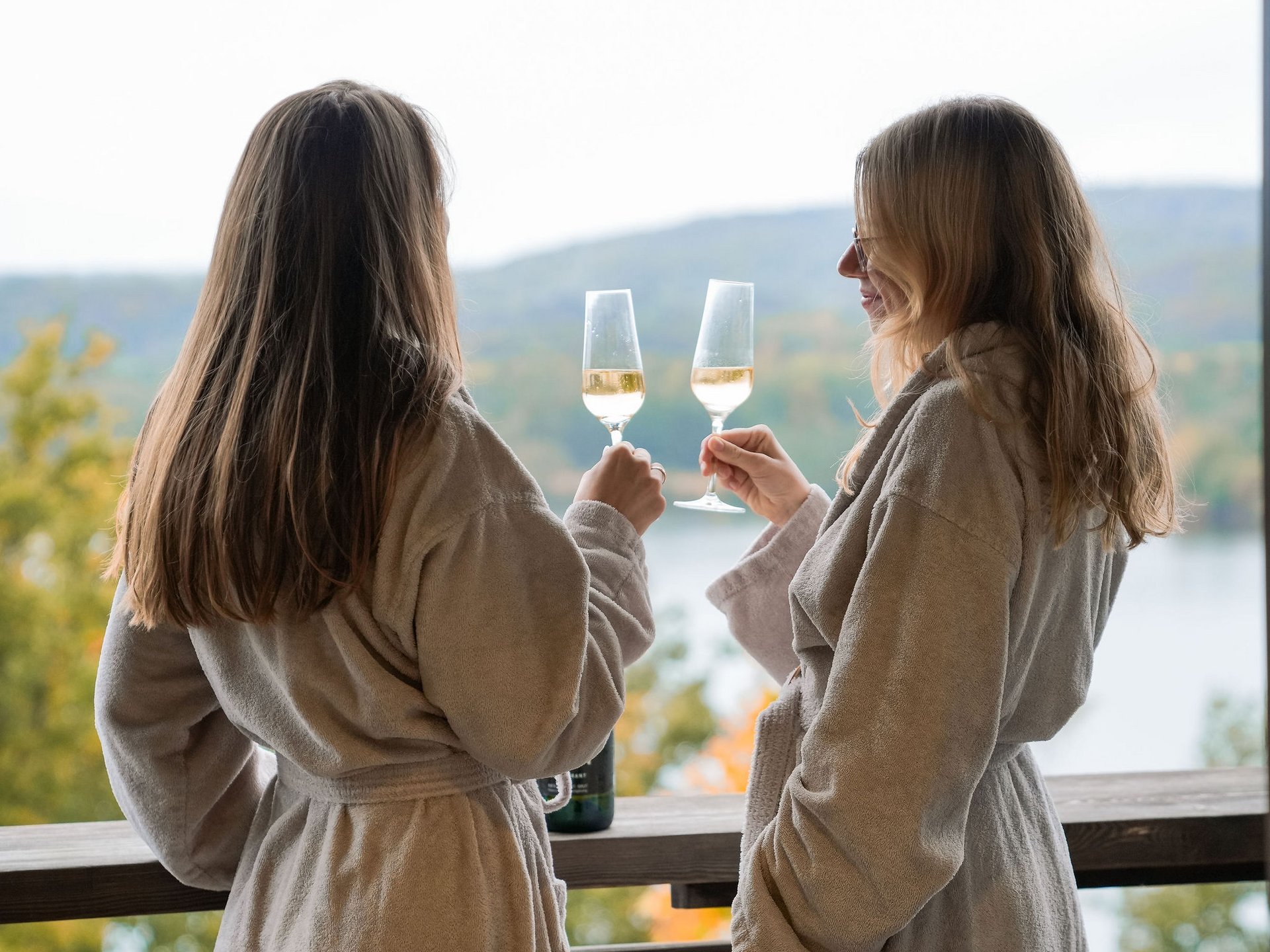 Zwei Frauen in Bademänteln stoßen mit Weingläsern auf einer Terrasse an