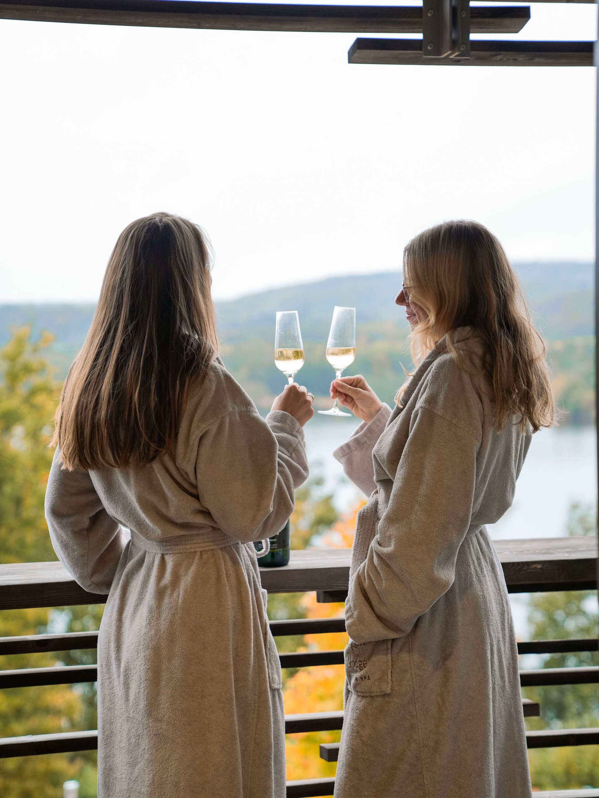 Zwei Frauen in Bademänteln stoßen mit Weingläsern auf einer Terrasse an
