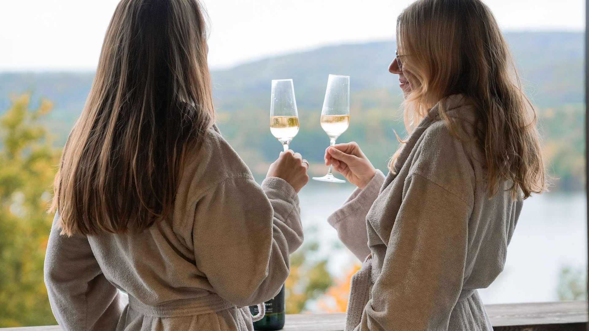 Deux femmes en peignoirs trinquent avec des verres de vin sur une terrasse