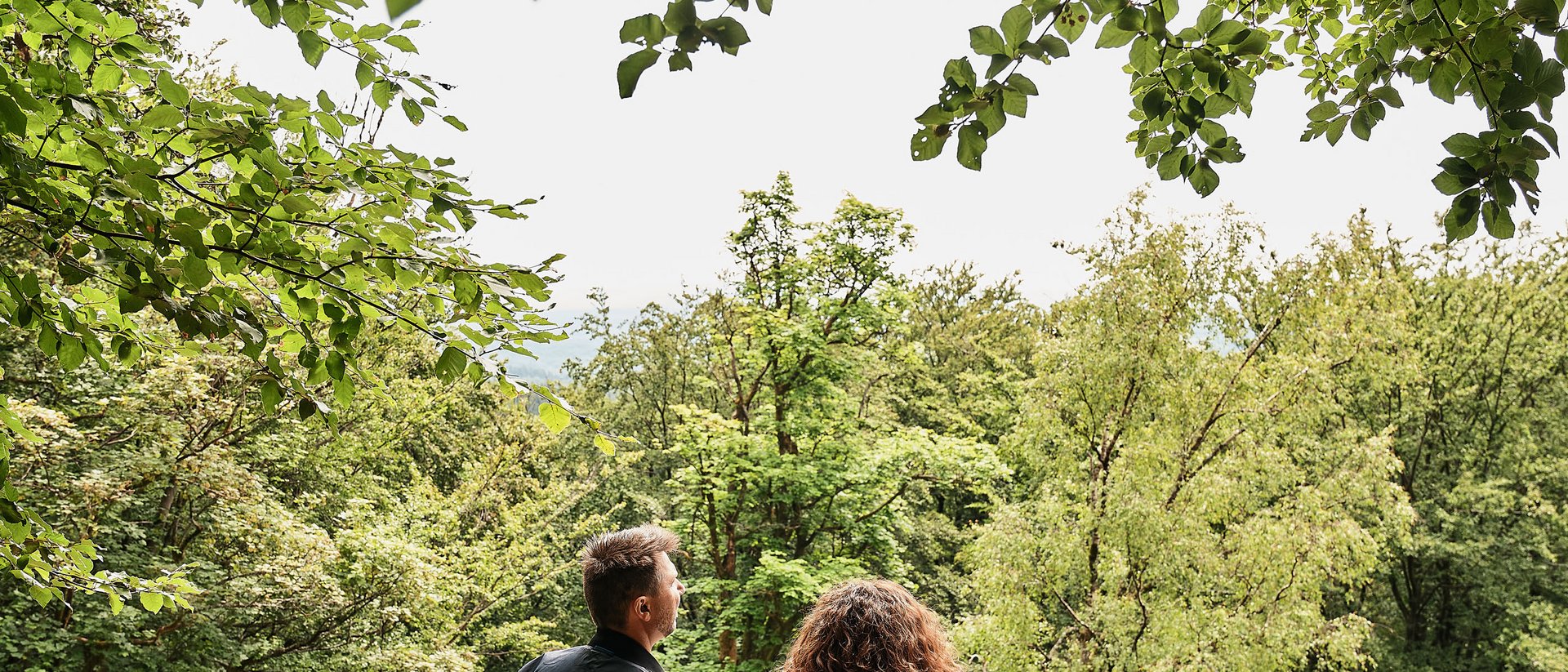 Paar steht im Wald und blickt auf Bäume und Natur