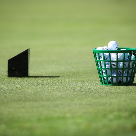 Grüner Korb voller Golfbälle auf Gras mit schwarzem Dartpfeil im Hintergrund
