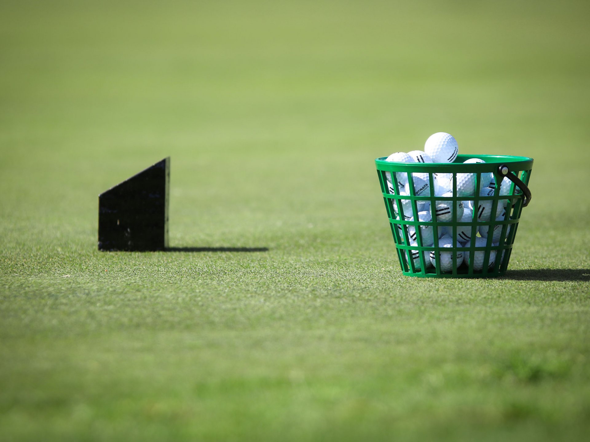 Grüner Korb voller Golfbälle auf Gras mit schwarzem Dartpfeil im Hintergrund