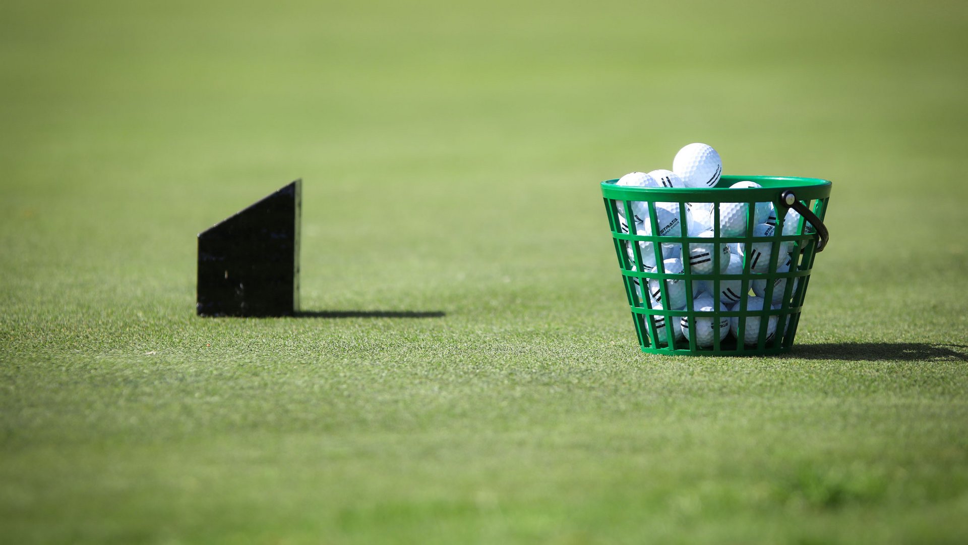 Grüner Korb voller Golfbälle auf Gras mit schwarzem Dartpfeil im Hintergrund