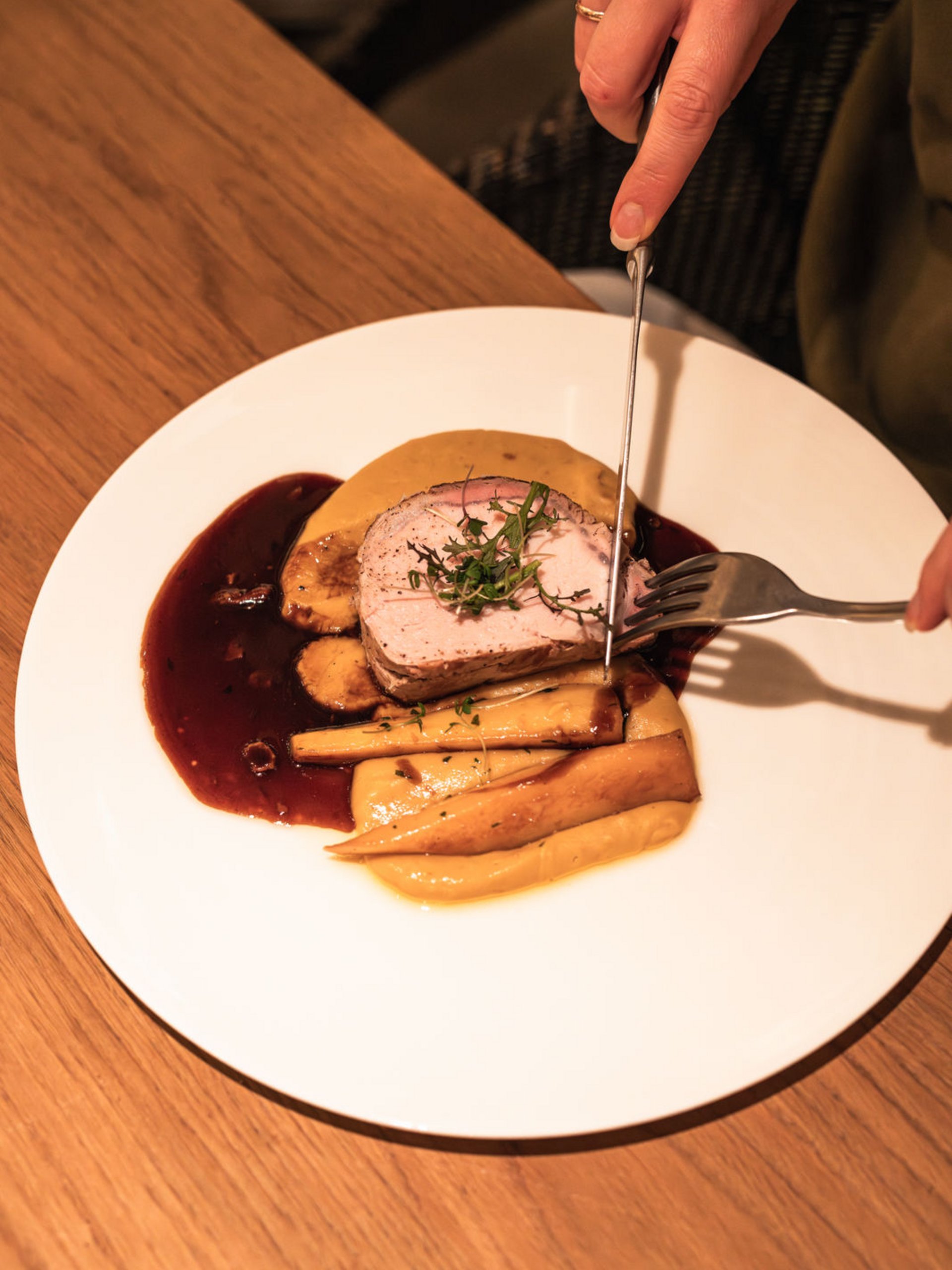 Person carving roasted meat with sides and sauce on a white plate