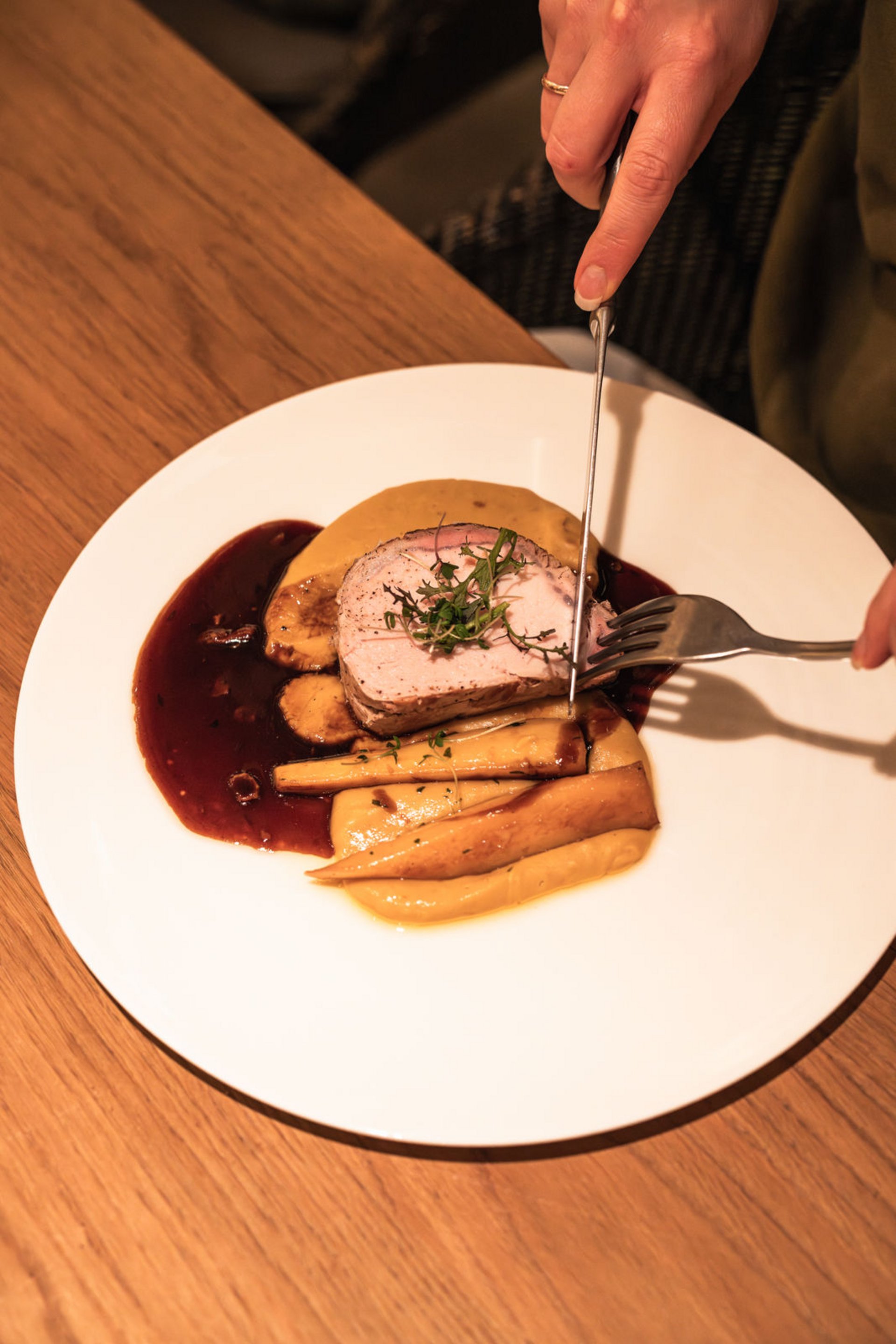 Person carving roasted meat with sides and sauce on a white plate