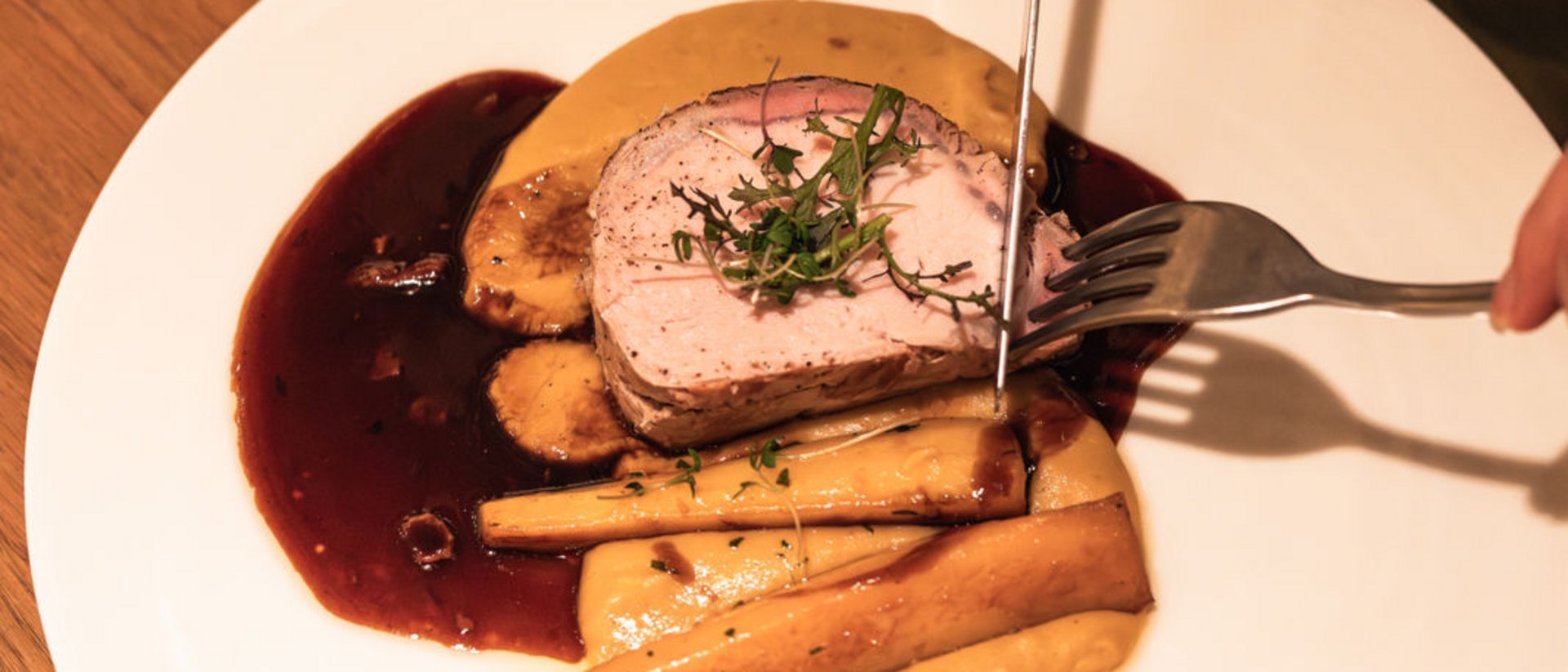 Person carving roasted meat with sides and sauce on a white plate