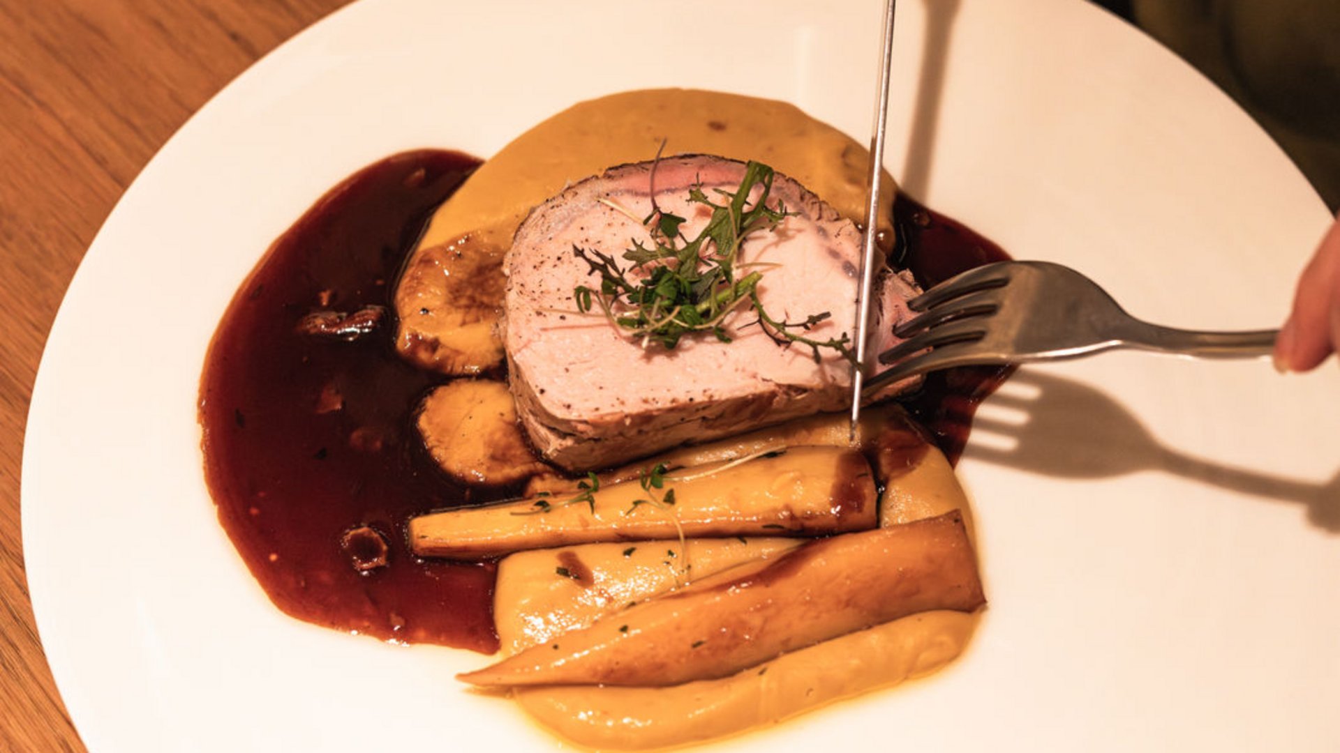 Person carving roasted meat with sides and sauce on a white plate