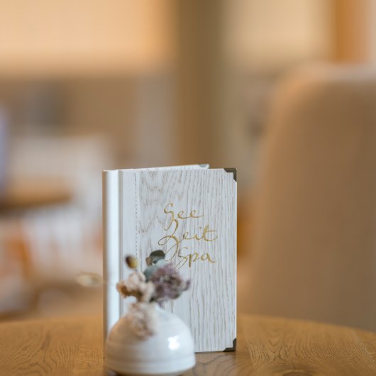 Weißes Spa-Menü und kleine Vase mit Trockenblumen auf Holztisch