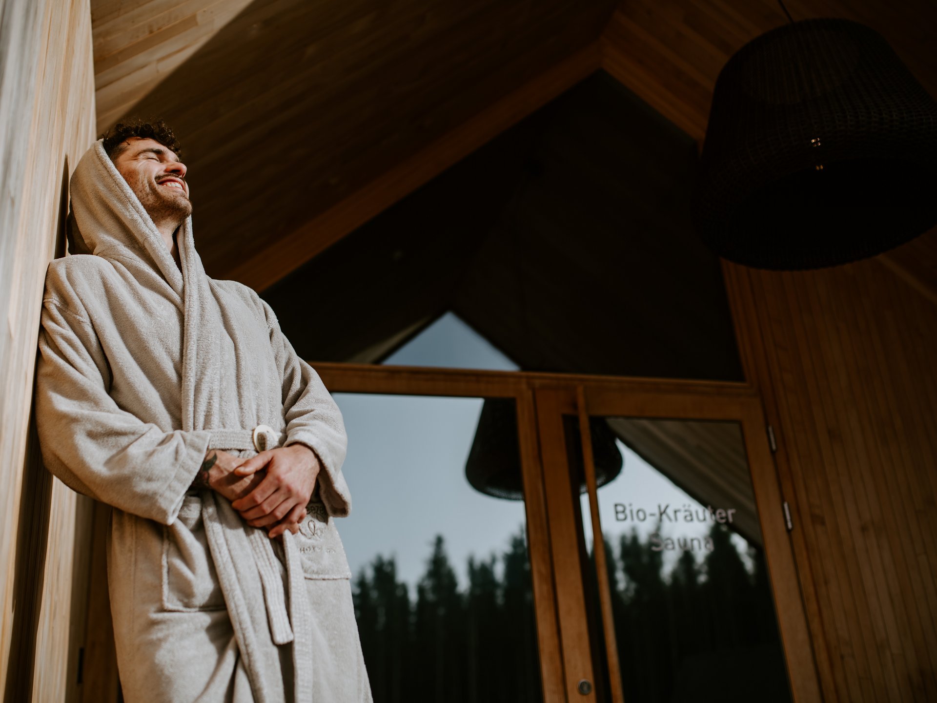 Mann in Bademantel entspannt vor Sauna-Tür im Holzhaus