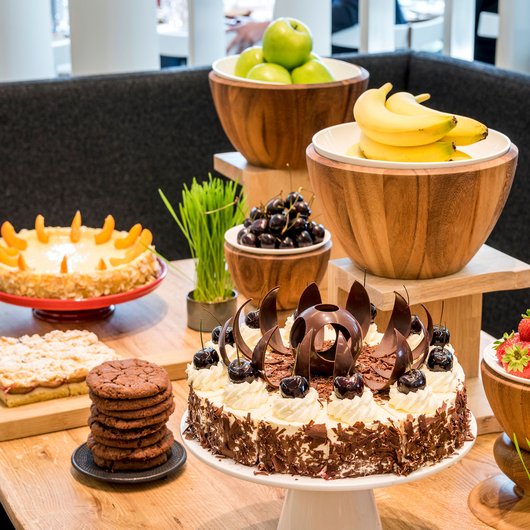 Tisch mit verschiedenen Kuchen, Keksen und frischem Obst in Holzschalen