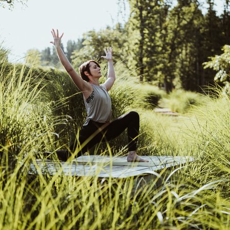 Frau praktiziert Yoga-Übung im Freien auf Matte inmitten grüner Pflanzen