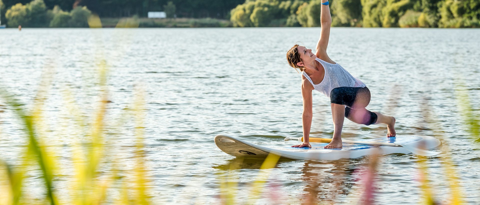 Frau macht Yoga auf einem Paddleboard auf einem See vor bewaldetem Ufer