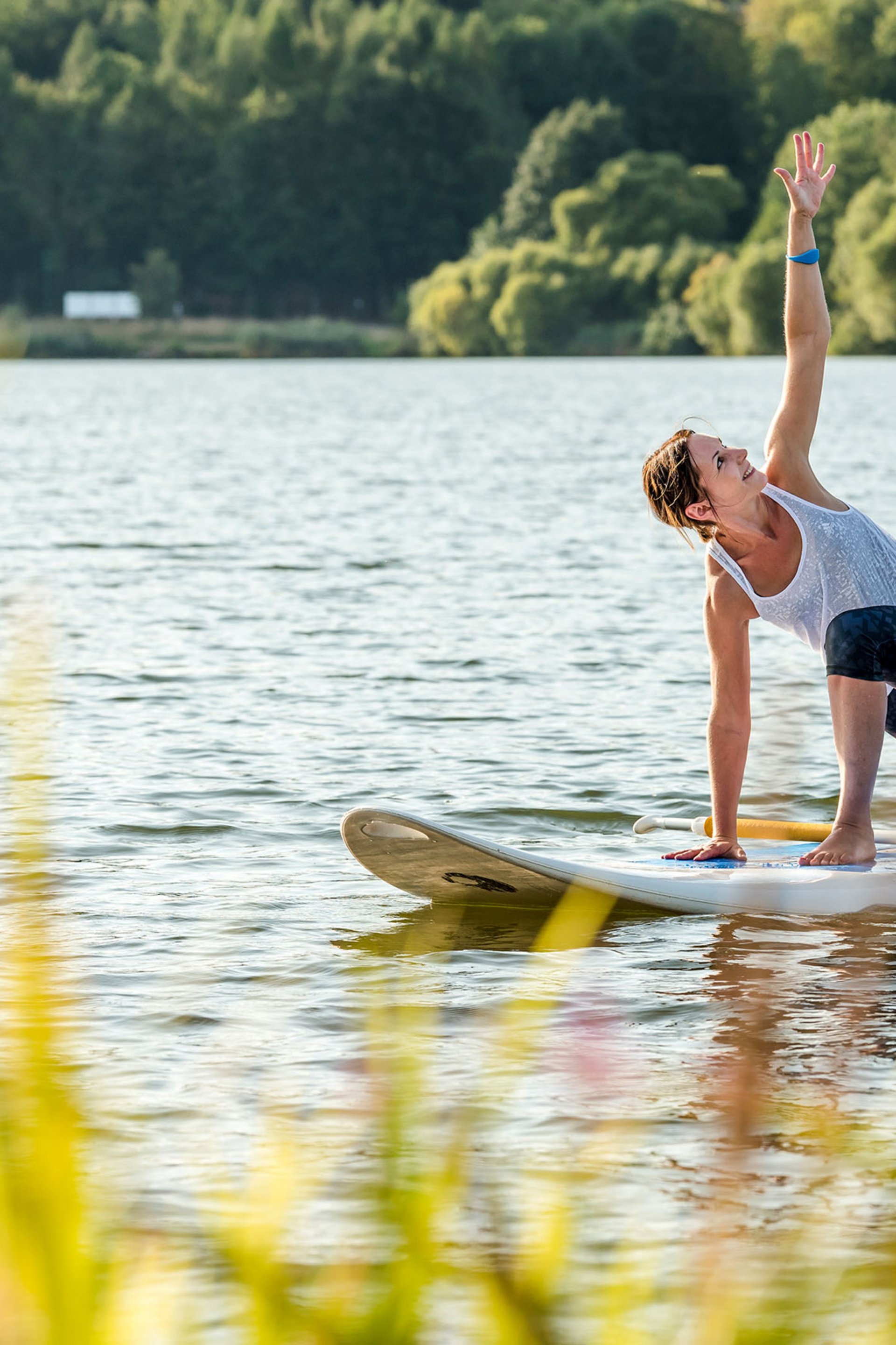Frau macht Yoga auf einem Paddleboard auf einem See vor bewaldetem Ufer