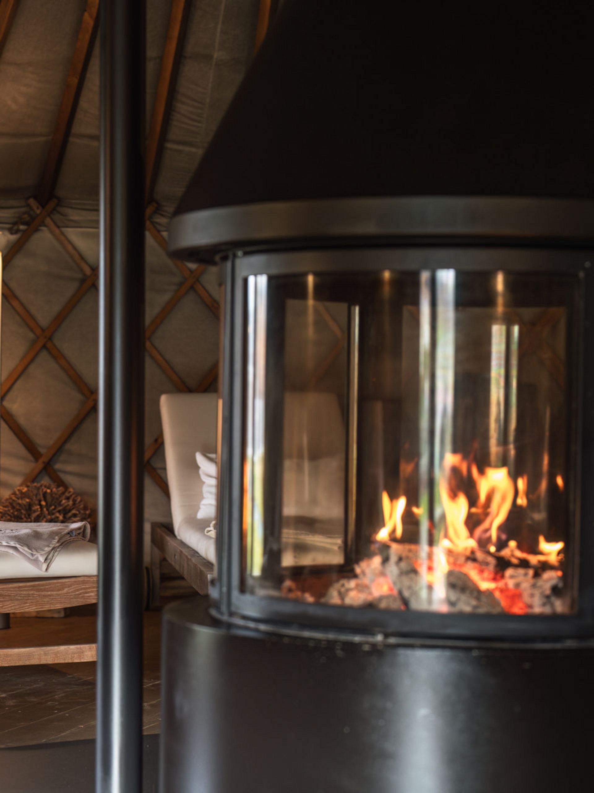 Fire burning in fireplace with cushioned wooden lounge chairs in cozy room