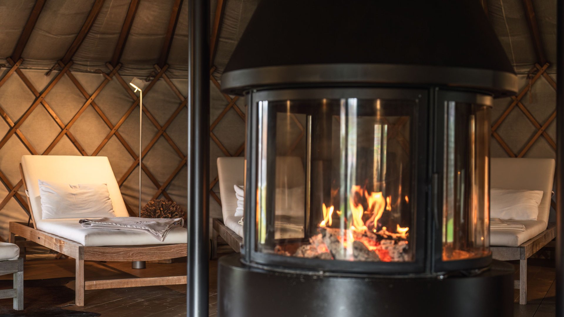 Fire burning in fireplace with cushioned wooden lounge chairs in cozy room