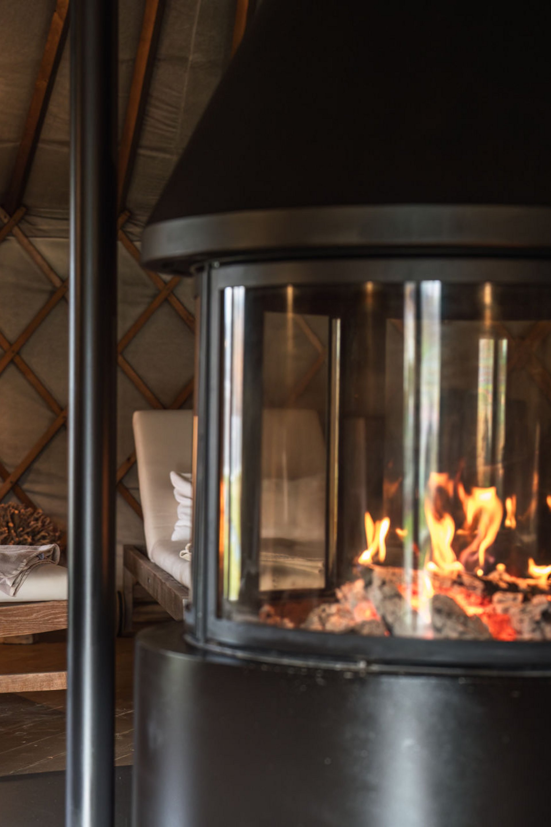 Fire burning in fireplace with cushioned wooden lounge chairs in cozy room