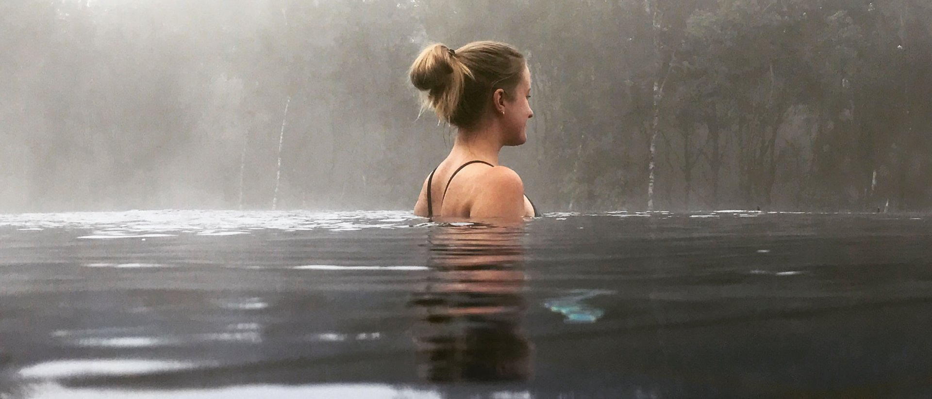 Femme se détendant dans l'eau avec brouillard et arbres en arrière-plan