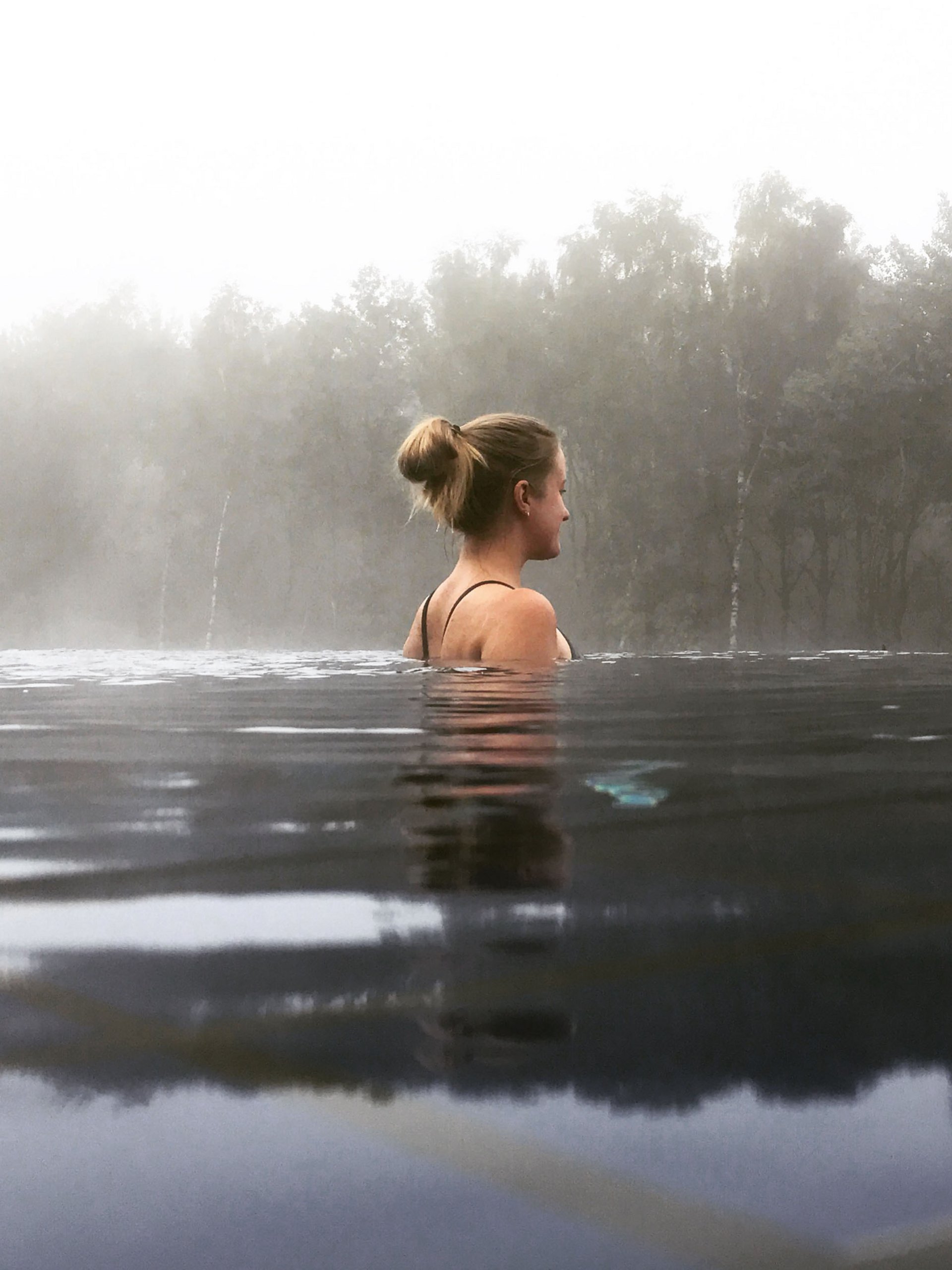 Frau entspannt im Wasser mit Nebel und Bäumen im Hintergrund