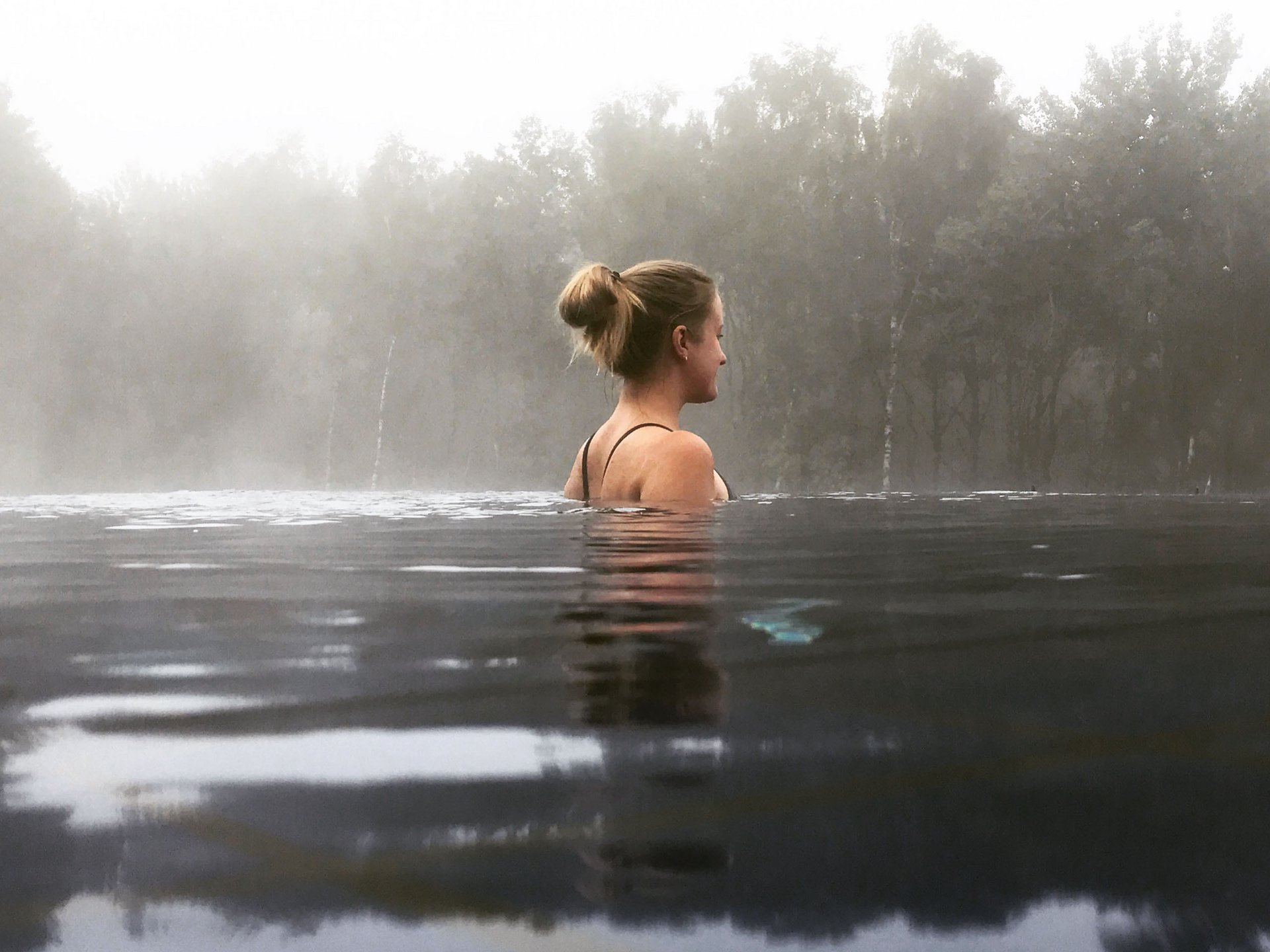 Femme se détendant dans l'eau avec brouillard et arbres en arrière-plan