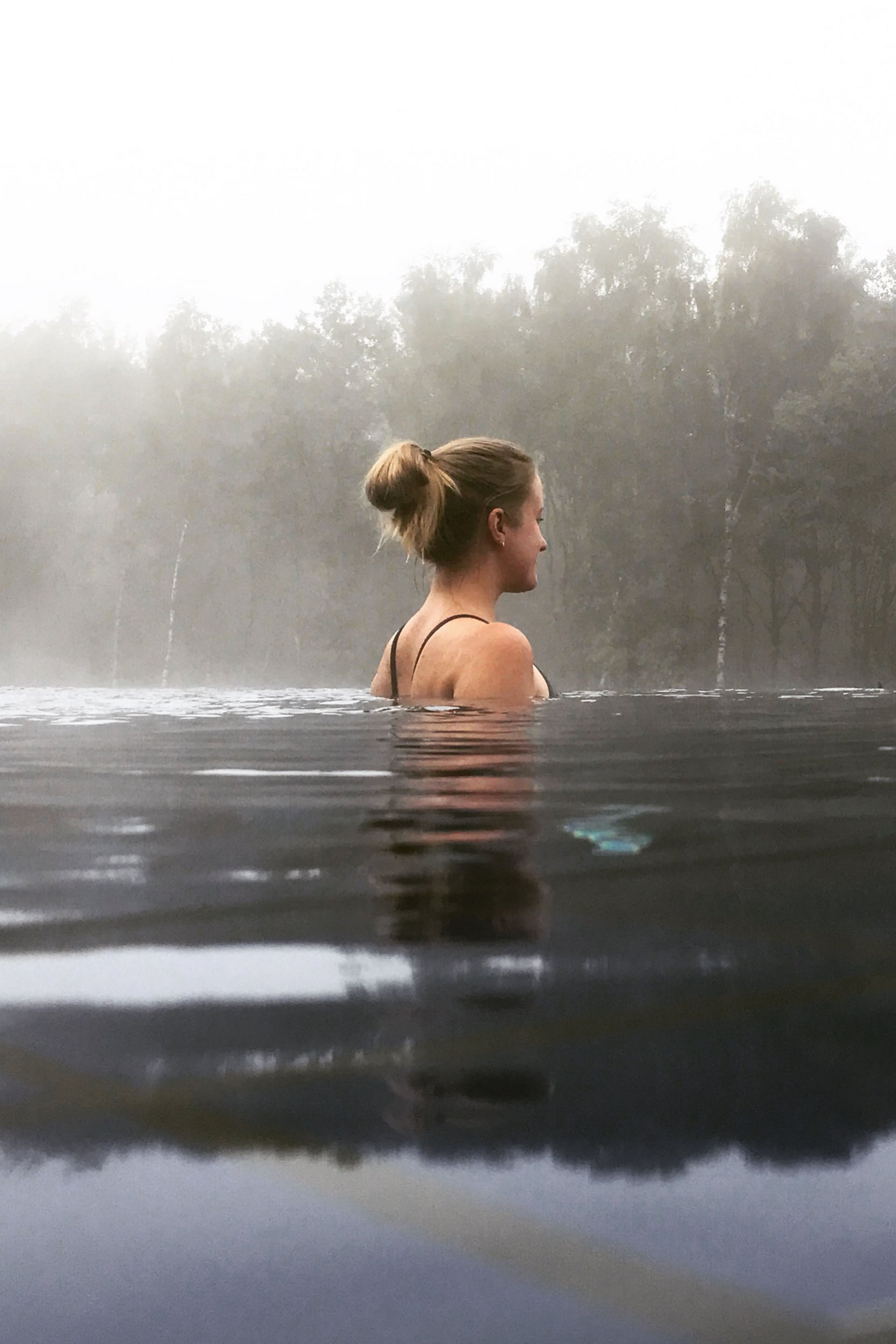 Femme se détendant dans l'eau avec brouillard et arbres en arrière-plan