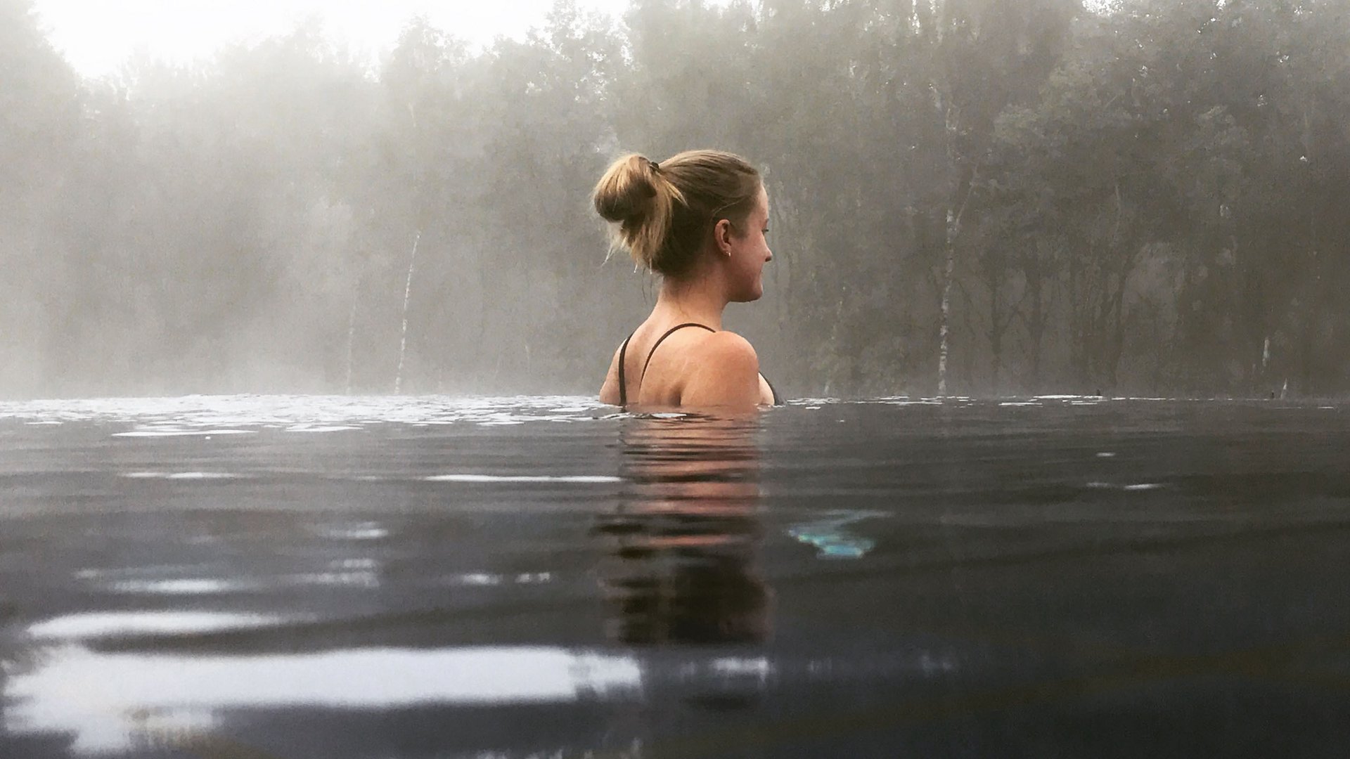 Femme se détendant dans l'eau avec brouillard et arbres en arrière-plan