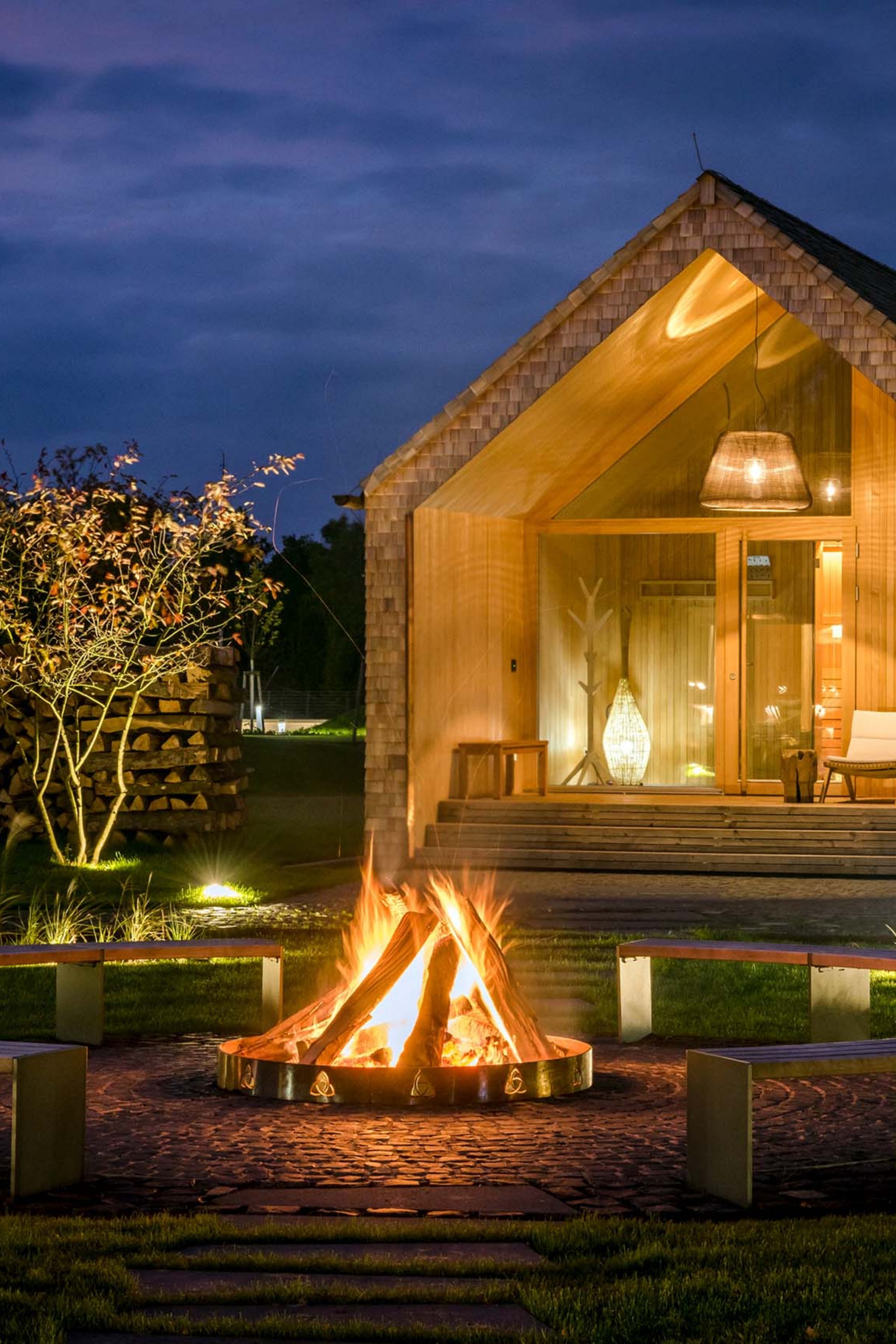 Wooden cabin at night with campfire and benches in the garden