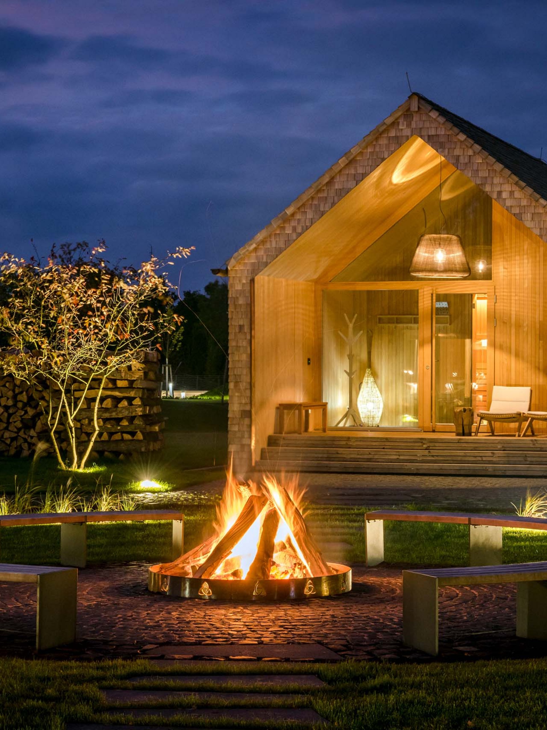 Maison en bois de nuit avec feu de camp et bancs dans le jardin