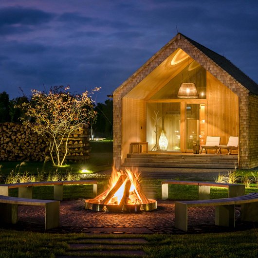 Wooden cabin at night with campfire and benches in the garden